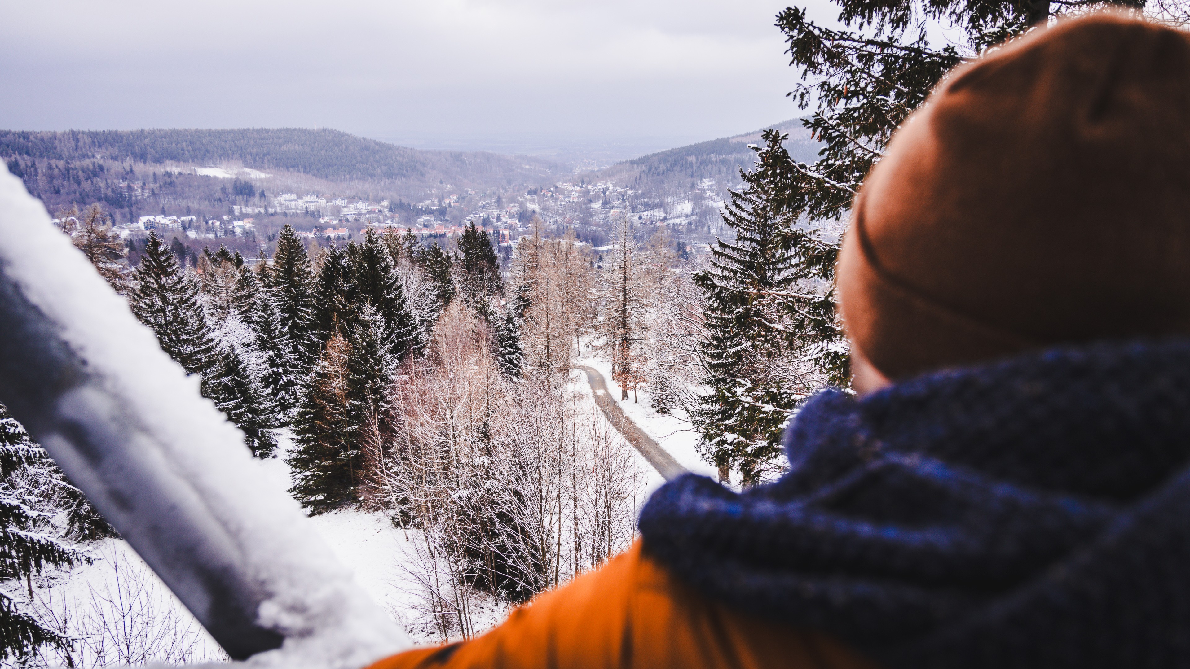 Zdjęcie przedstawia osobę w zimowej czapce i kurtce, stojącą tyłem do widza i patrzącą na zaśnieżony, górzysty krajobraz.